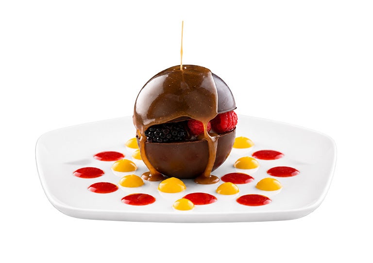 Postre con cobertura de chocolate relleno de frutas sobre plato con decoraciones de salsa