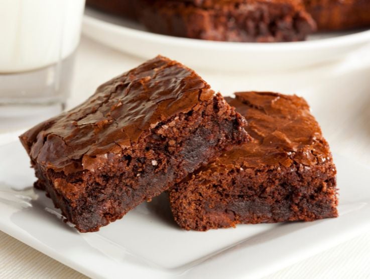 Porciones de brownie de chocolate denso servidas sobre un plato cuadrado de porcelana blanca.