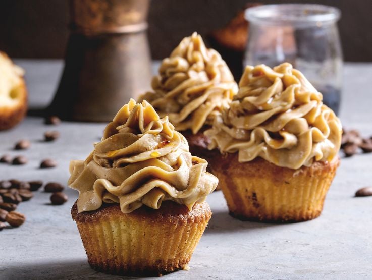 Cupcakes dulces con un betún cremoso de café dispuestos en una superficie con granos secos.