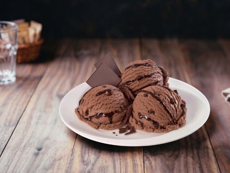 Tres bolas de helado de chocolate con jarabe de café y trozos crujientes sobre un plato blanco.