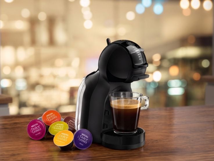 Máquina de café con cápsulas y taza de café sobre mesa de madera