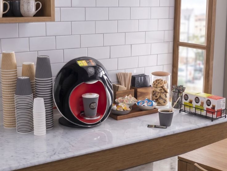 Máquina de café con taza servida en encimera junto a vasos y galletas
