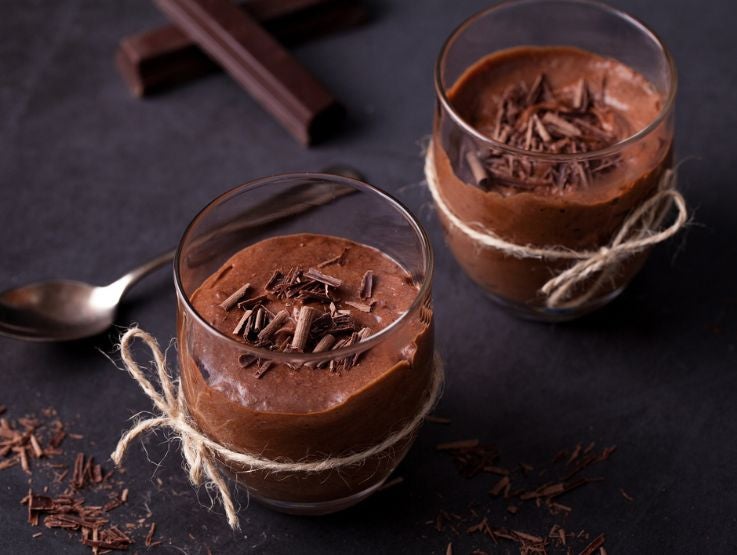 Vasos de vidrio con mousse de chocolate cremoso decorado con virutas finas sobre fondo oscuro.