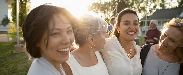 Grupo de mujeres abrazadas sonriendo al aire libre durante una actividad comunitaria