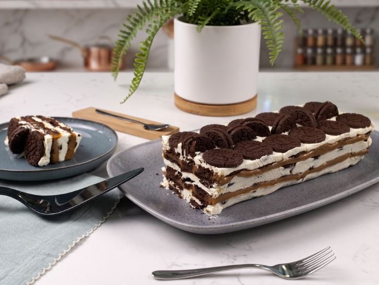 Pastel helado de capas con crema, manjar y galletas de chocolate servido sobre un plato gris.