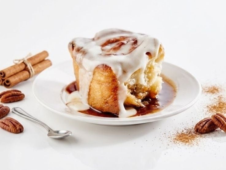 Rollo de canela esponjoso cubierto con abundante glaseado blanco sobre un plato de cerámica.